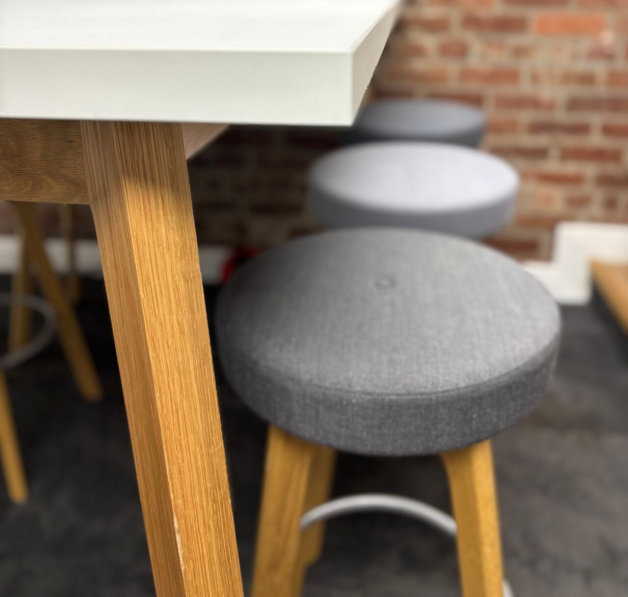 White table and gray stools with light wood legs, set against a brick wall.