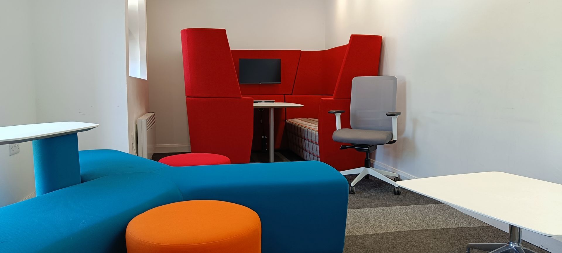 A modern office lounge with colorful seating and a red privacy booth.