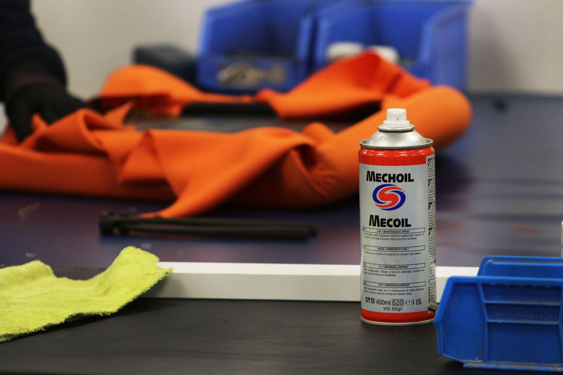 Can of Mecoil spray on a workbench, with orange cloth and blue bins.
