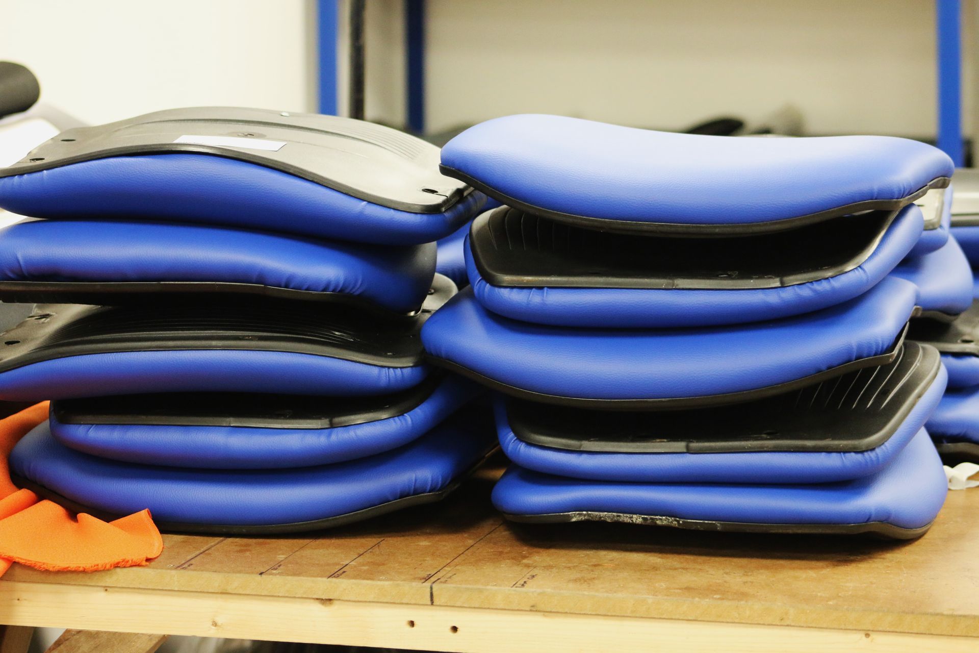 Stacks of blue cushioned seats on a wooden surface, with black undersides.