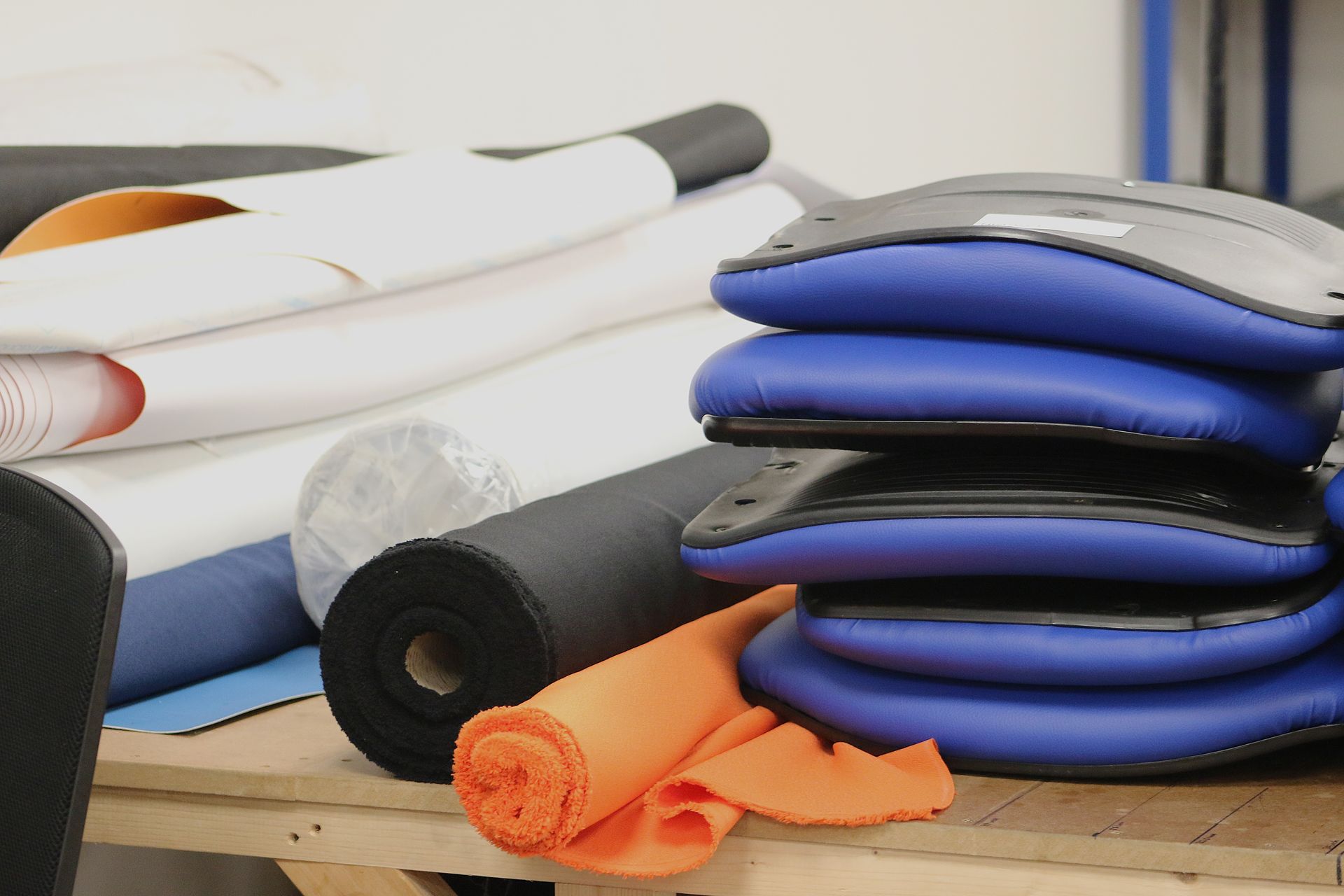 Rolls of fabric and stacked blue cushions on a wooden surface in a workshop.