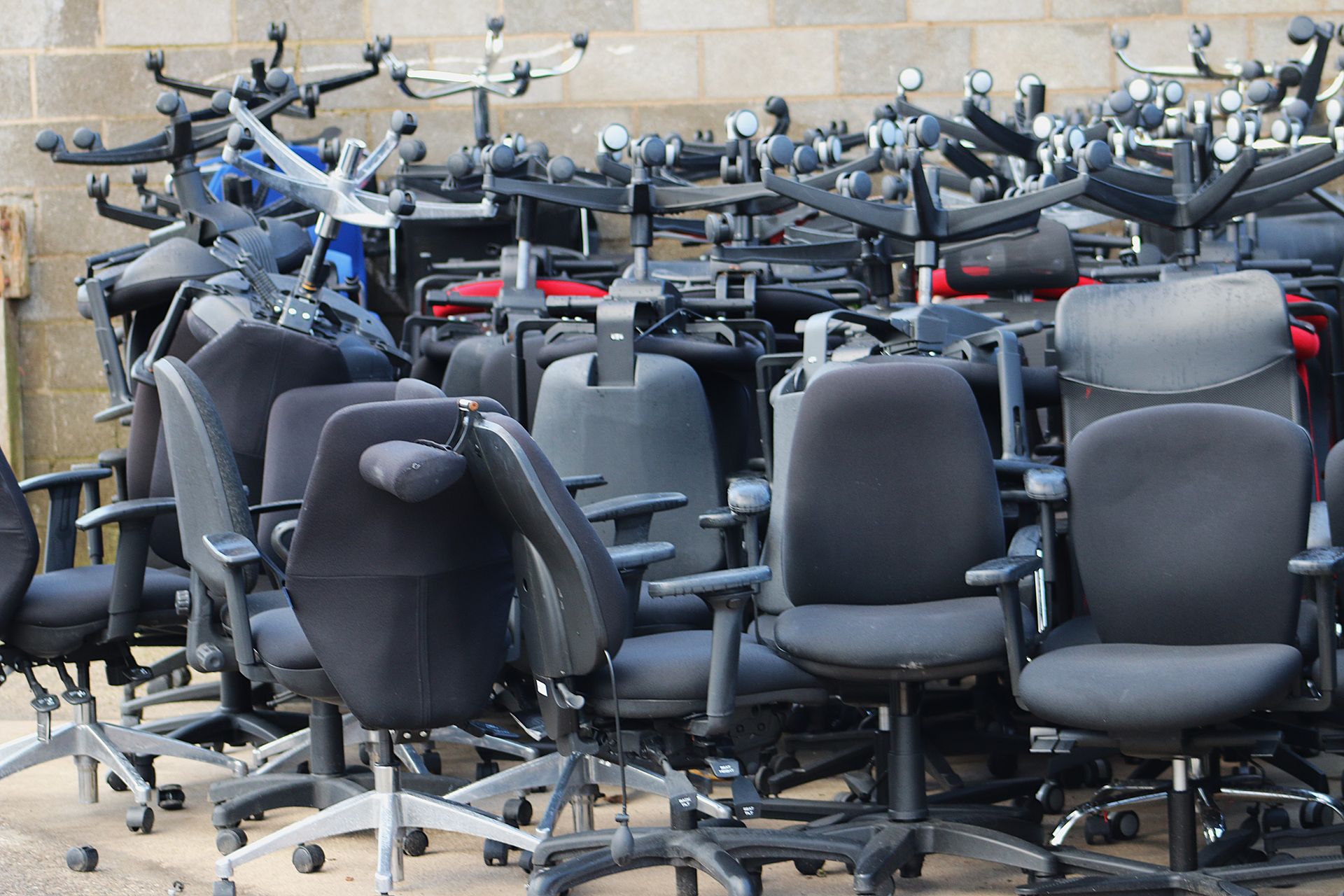 Pile of used office chairs, primarily black, in an outdoor setting.