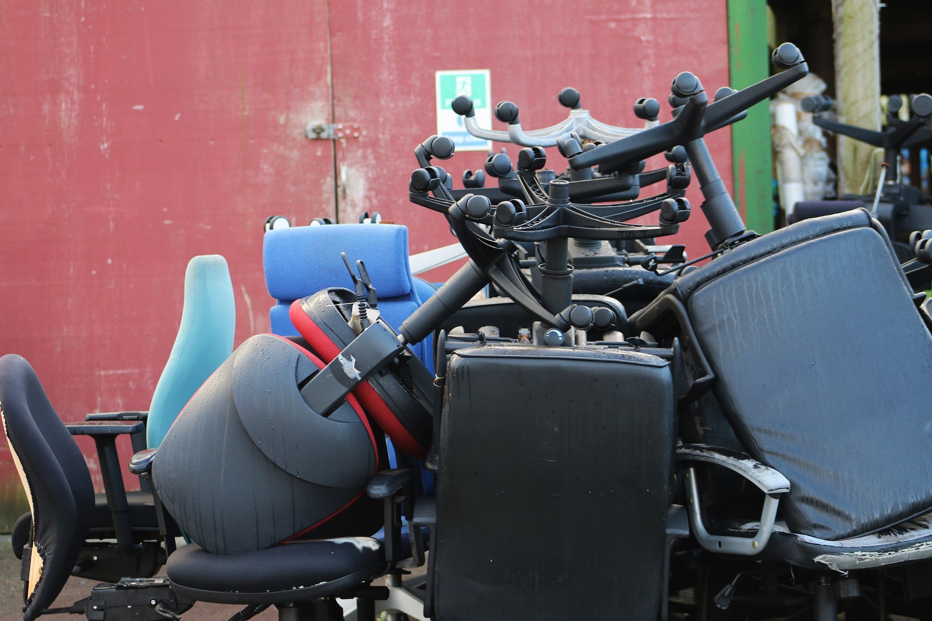 Pile of discarded office chairs against a red wall, with various colors and styles.