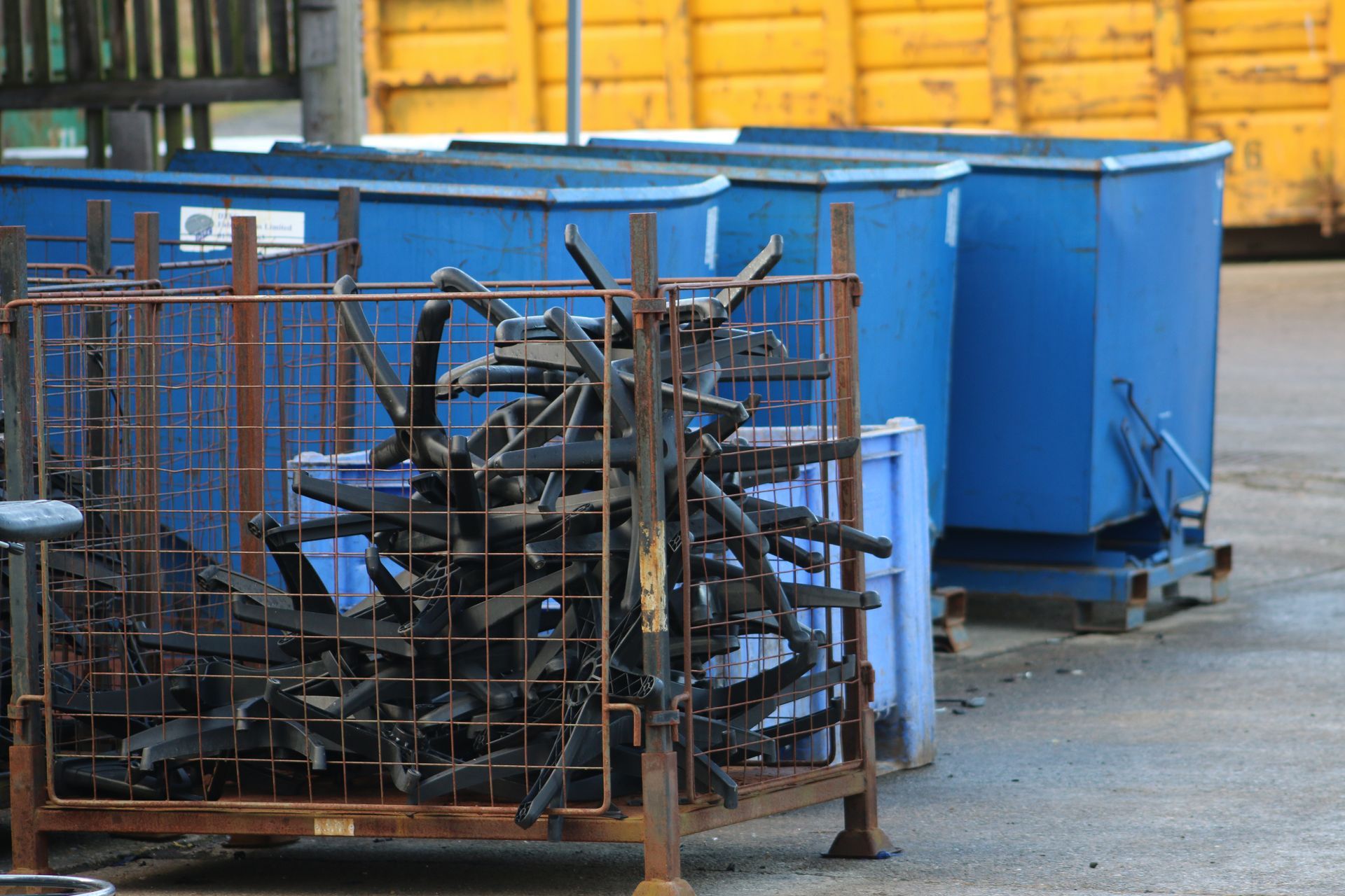 Metal scraps in a wire bin, with blue storage containers in the background. Industrial setting.