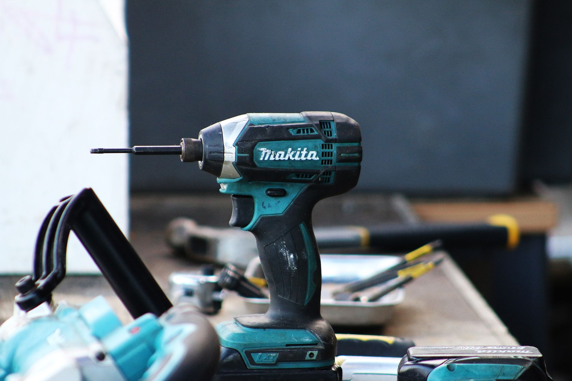 Makita teal and black cordless impact driver on a workbench with other tools.