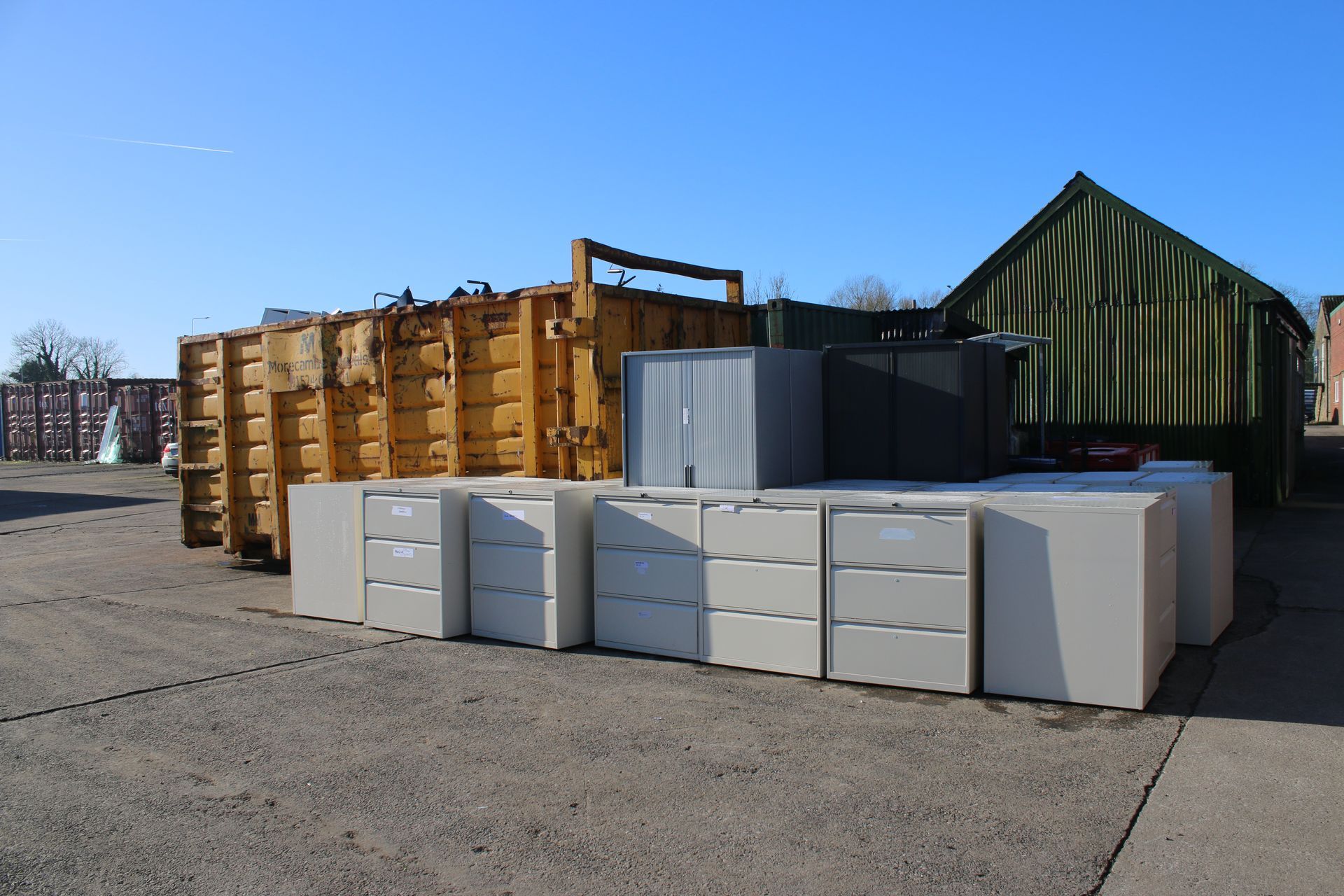 A junkyard scene with metal containers and white office storage units under a clear blue sky.