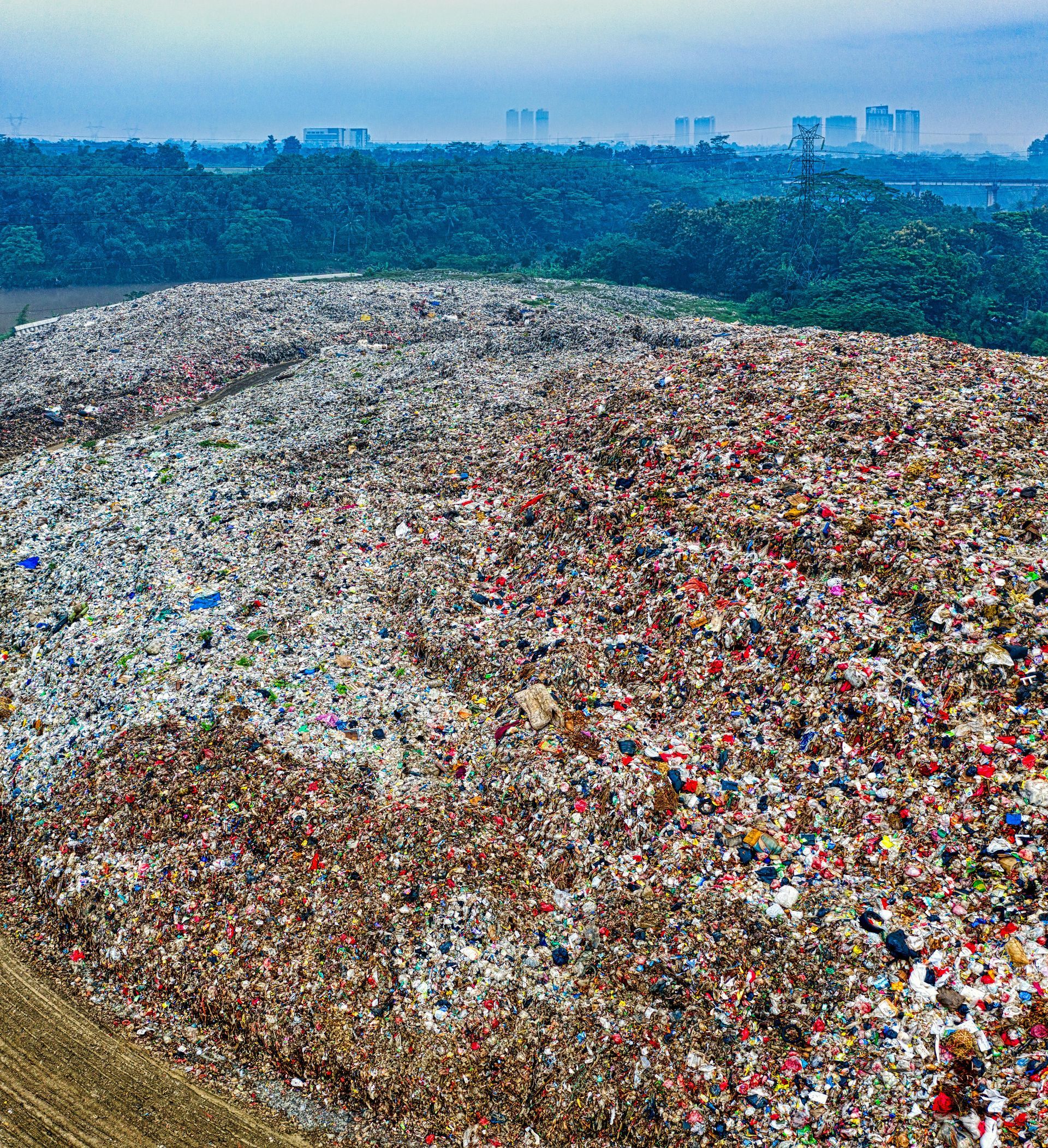 Large landfill mound in an outdoor setting, with buildings in the background and a forest in between.