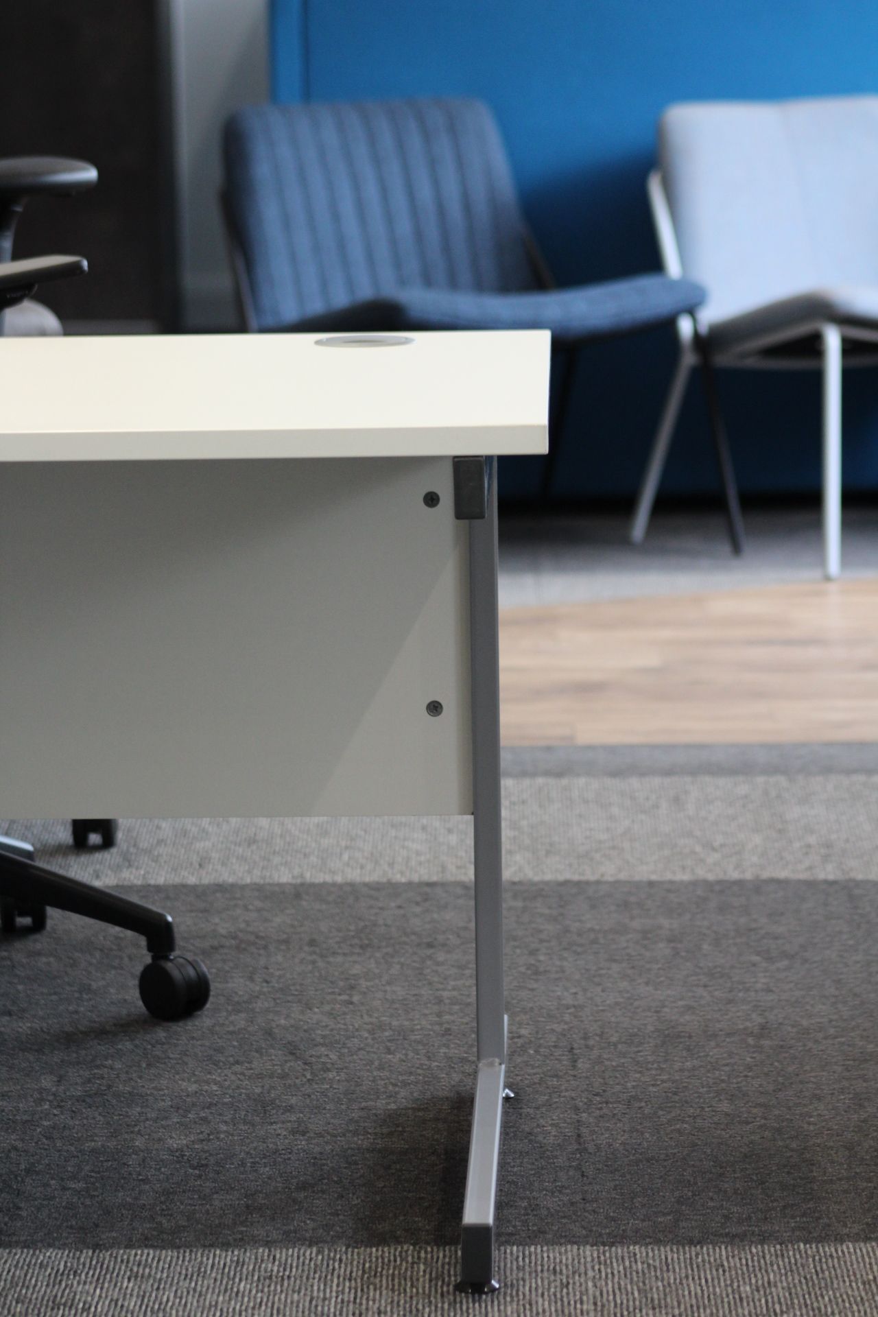 White desk with metal legs in office, gray carpet. Blue chairs in the background.