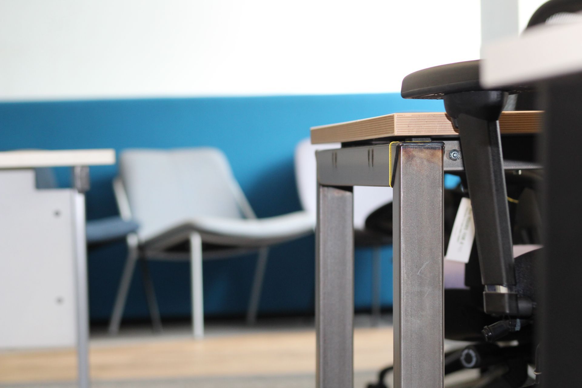 Office desk close-up with a chair. Blue and white walls, grey chair in the background.