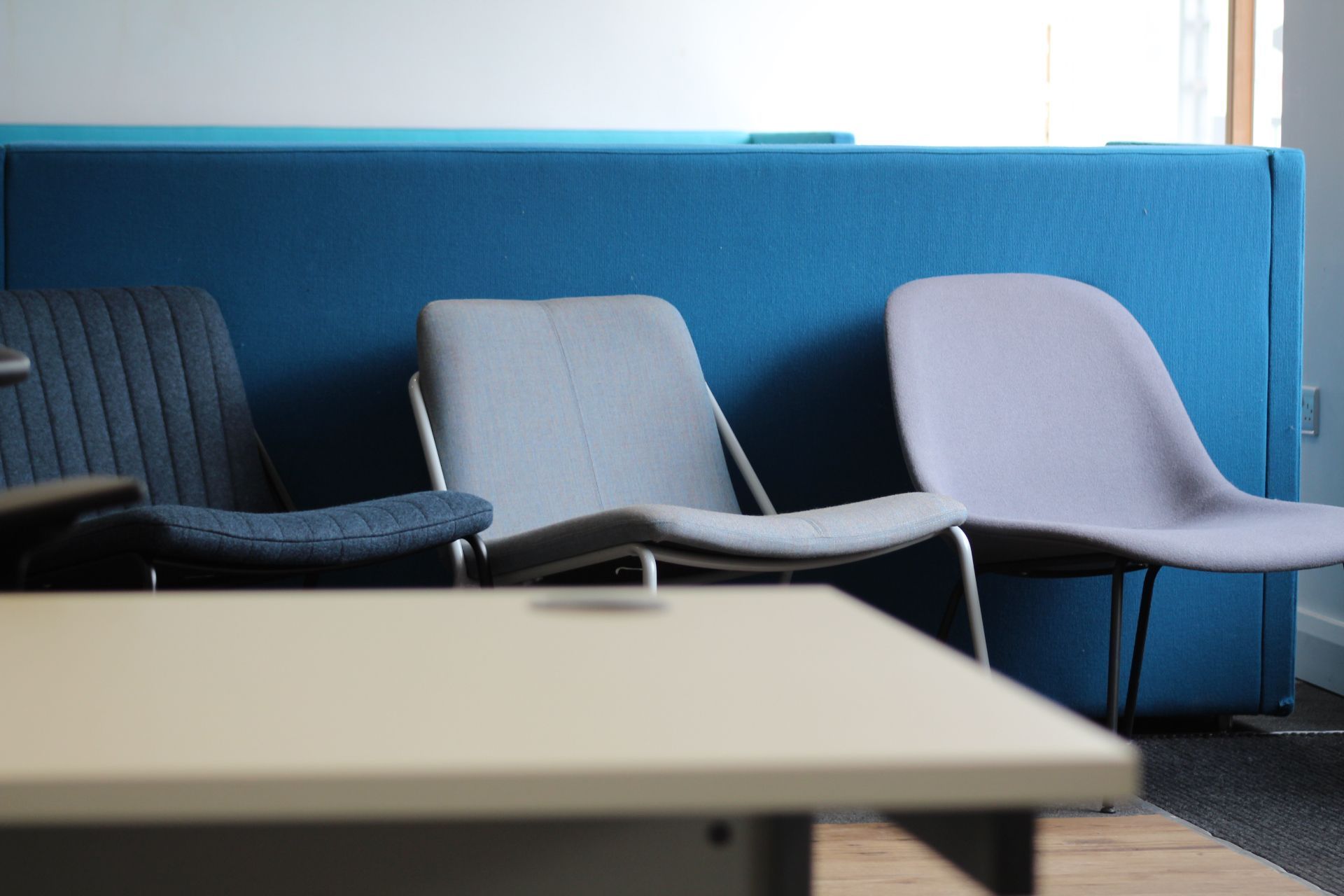 Three chairs in front of a blue padded wall, with a desk in the foreground.