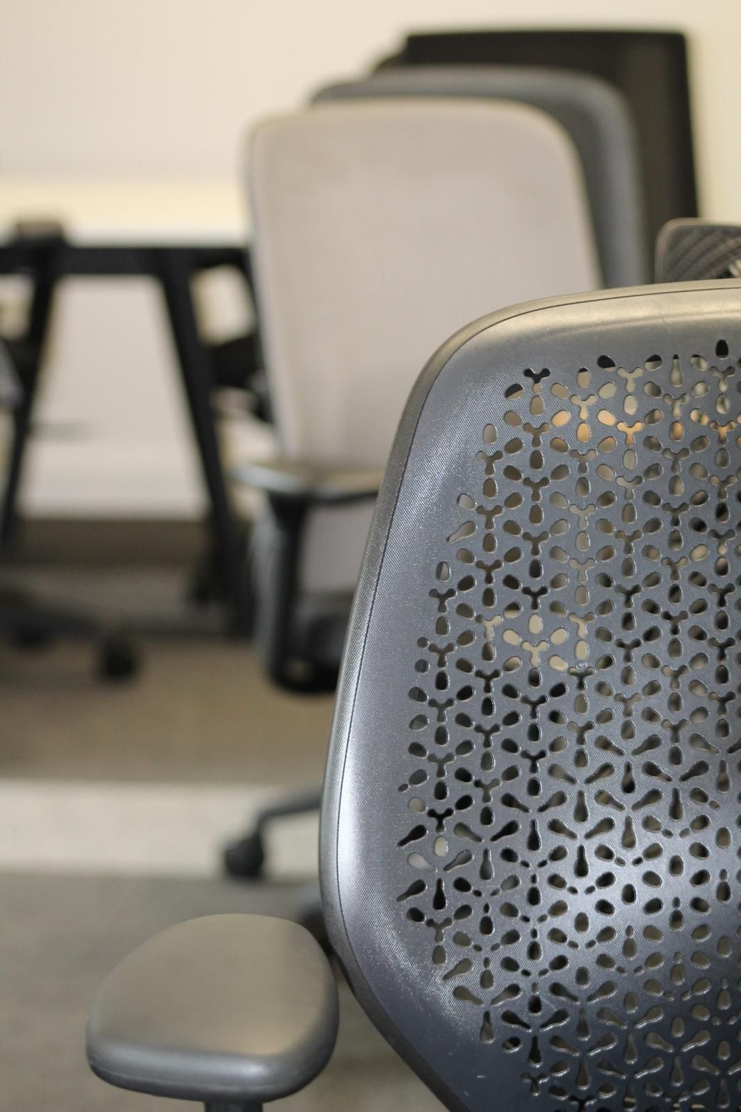 Office chairs lined up, focus on a gray chair with decorative back; other chairs blurred in background.