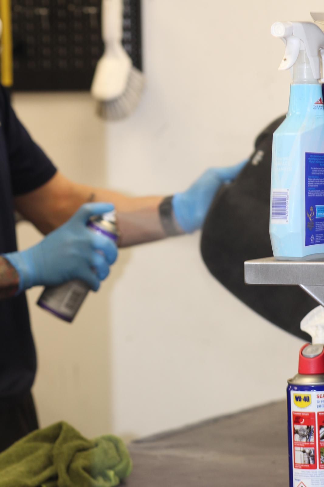Person in blue gloves spraying cleaning product on a black object.
