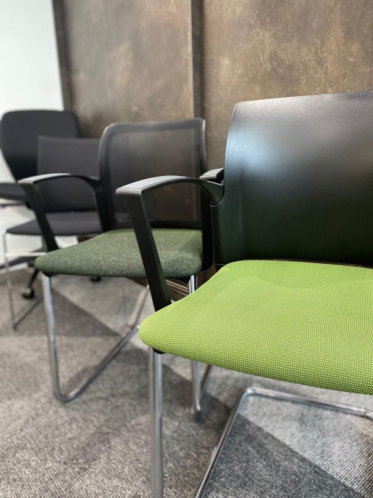 Row of office chairs with black backs and green seats against a textured gray wall.