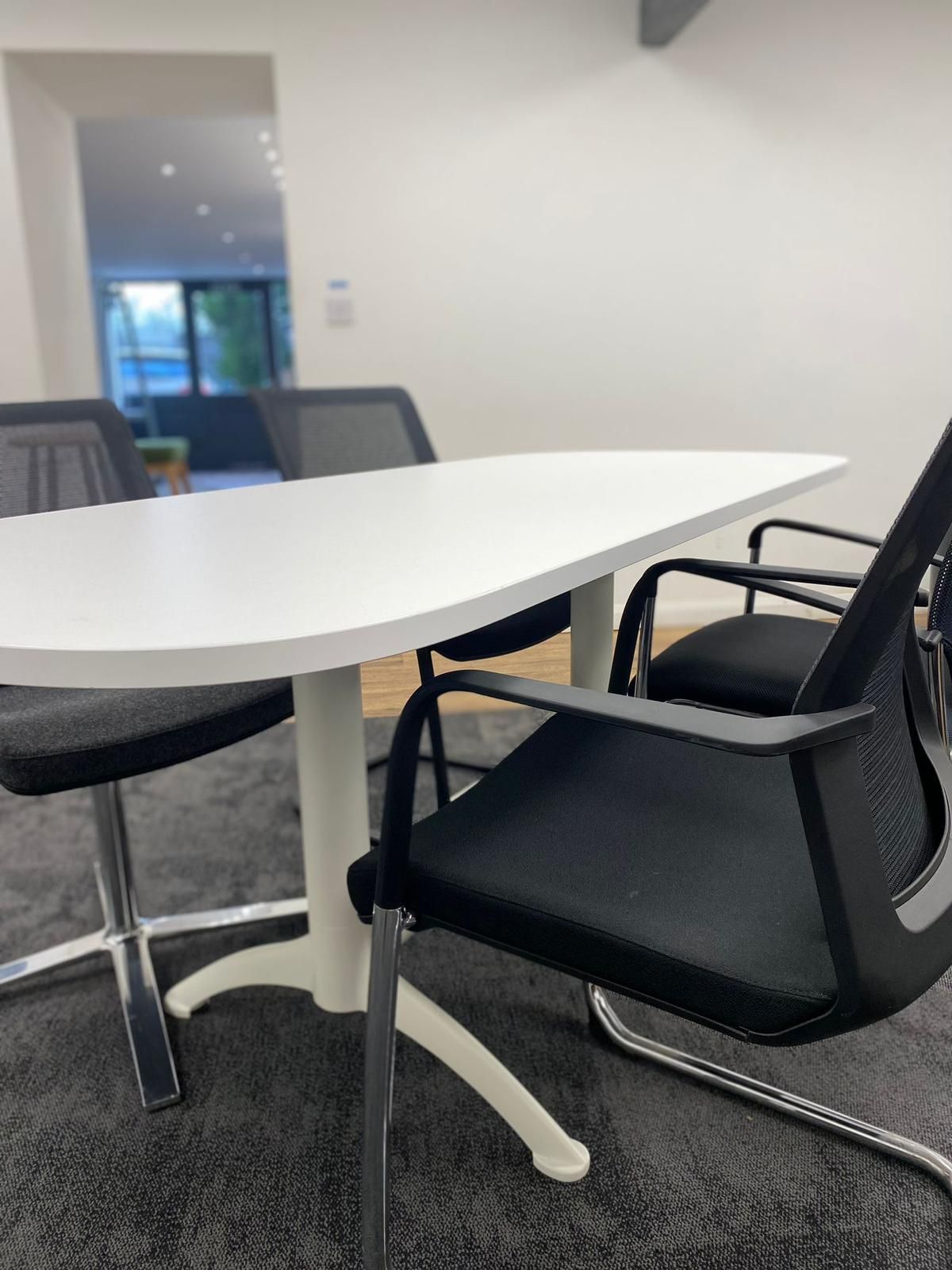 White table with three black chairs in a room with white walls and a carpeted floor.