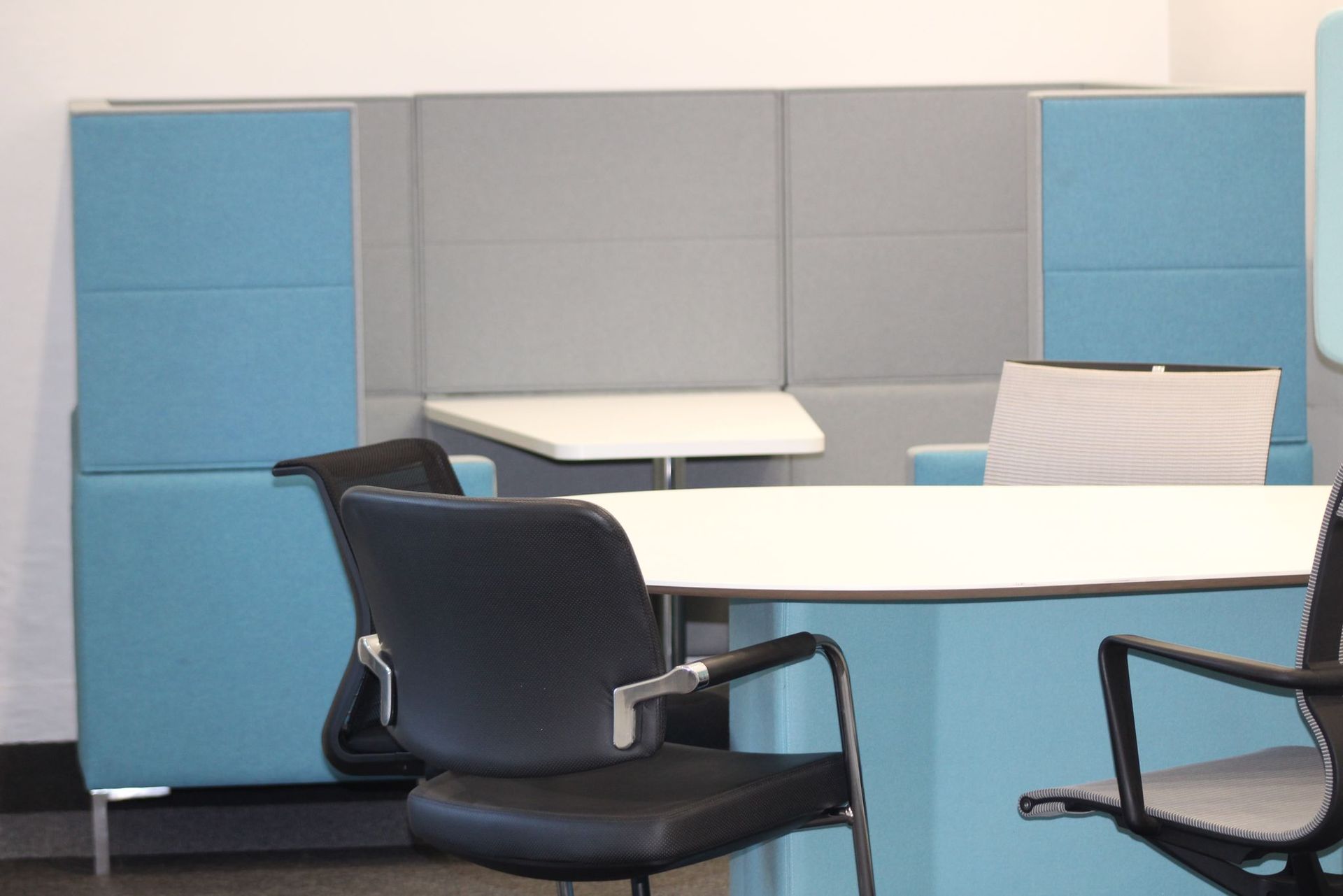 Office area with light blue and gray padded wall, white table, and black chairs.