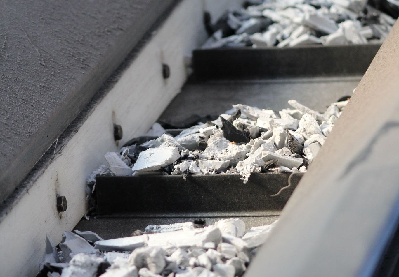 Conveyor belt with gray metal steps carrying fragmented white material, likely debris.