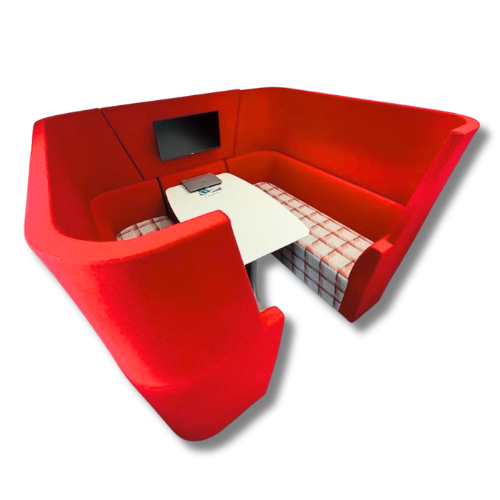 Red, booth-style seating with a table, monitor, and laptop, in a modern, open space.