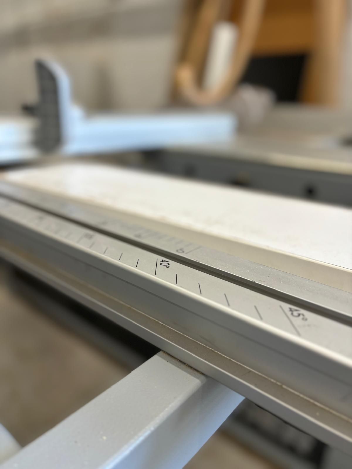 Close-up of a table saw fence with measurement markings; silver and gray.