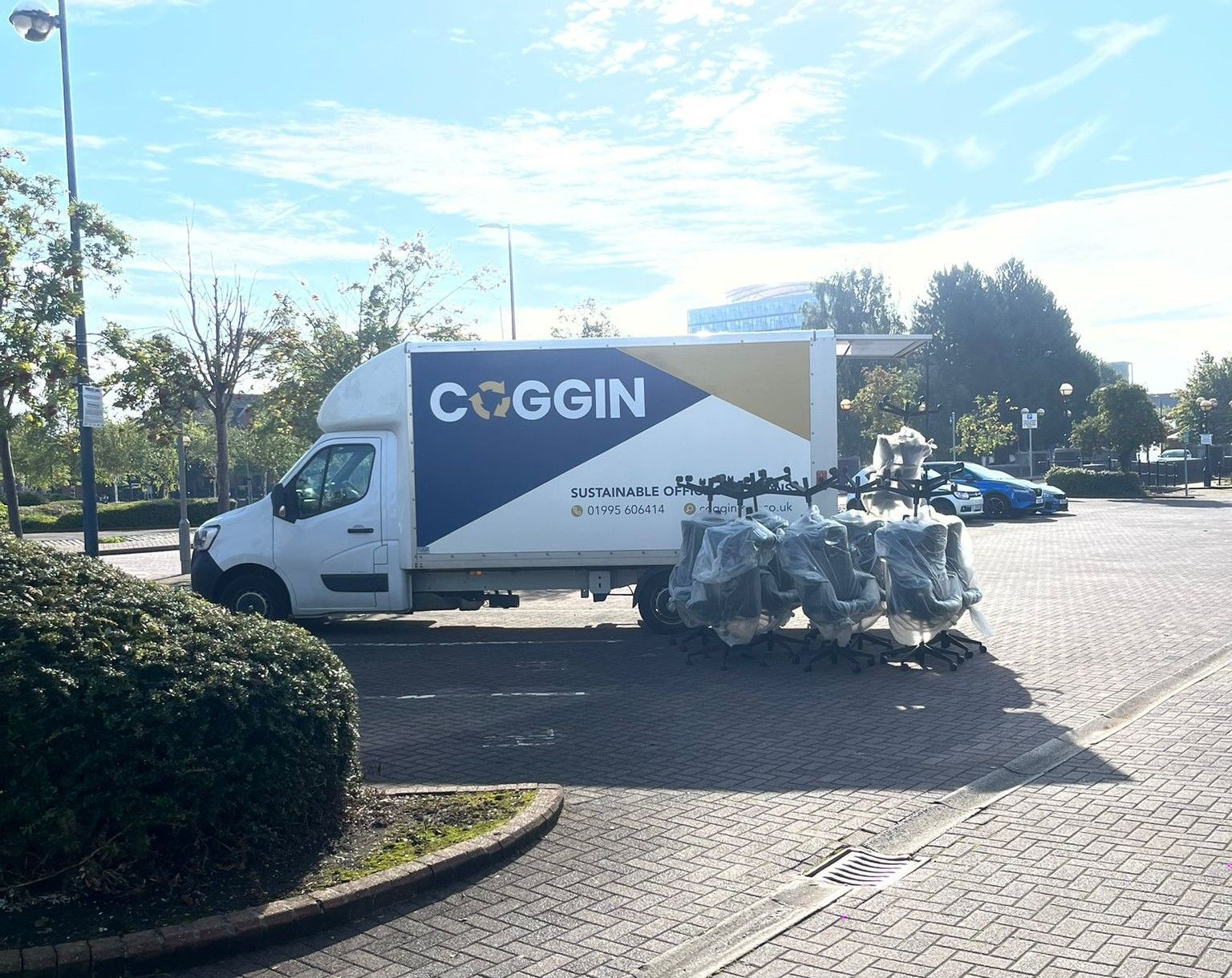 A white Coggin moving van parked in a paved lot; black objects are wrapped in plastic nearby.
