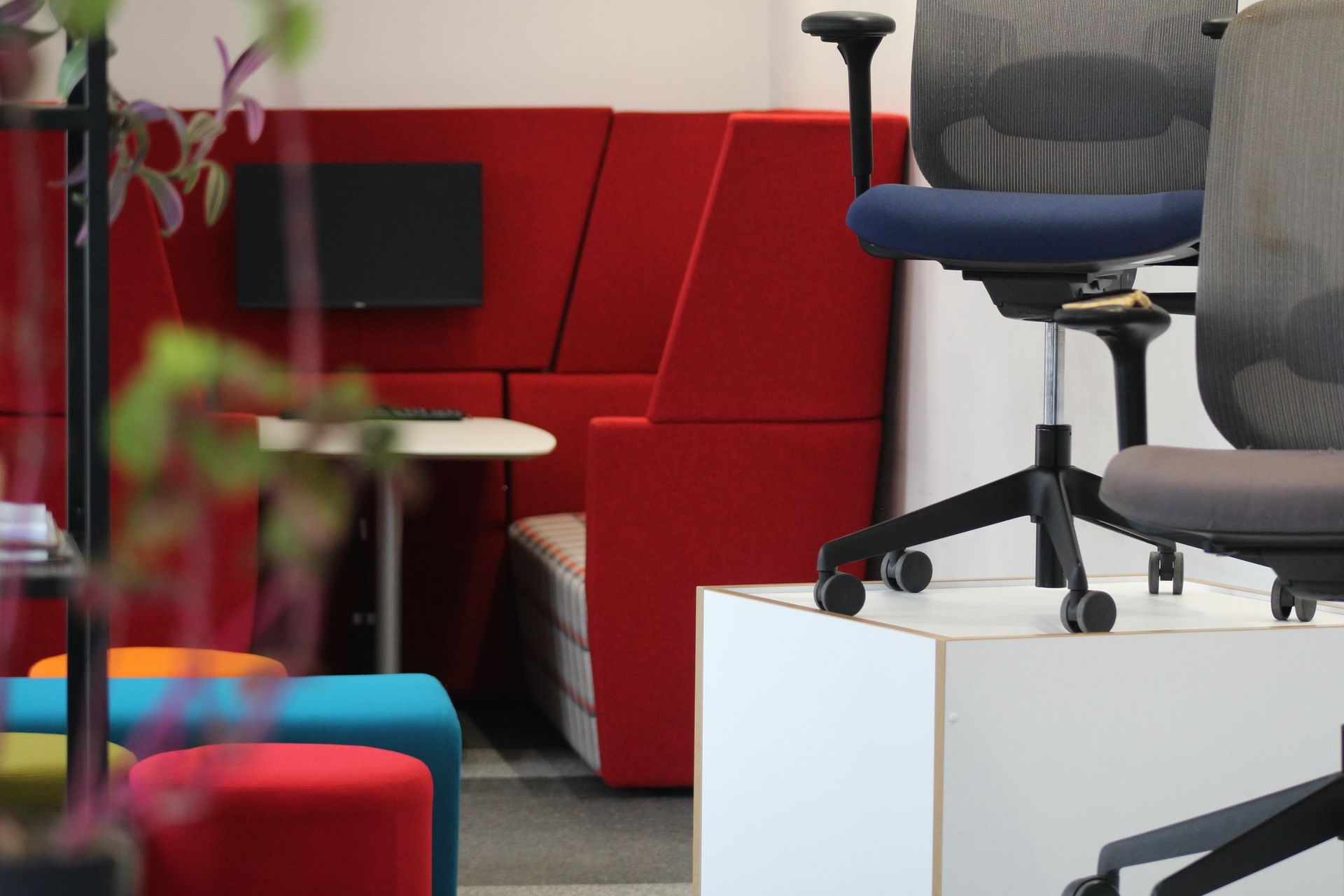 Office space with red booth, blue and gray chairs, colorful stools, and a small table.