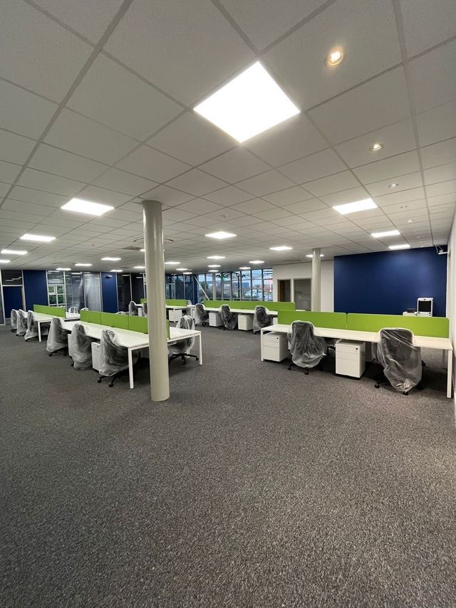 Refurbished bench desks with green screens, pedestals and task chairs installed in an open plan office
