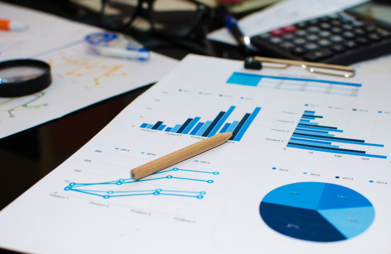 Graphs and charts on white paper with a pencil, calculator, and magnifying glass.