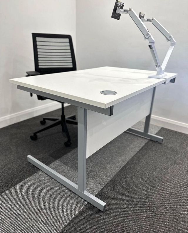 A single refurbished white desk with monitor arms and a mesh task chair