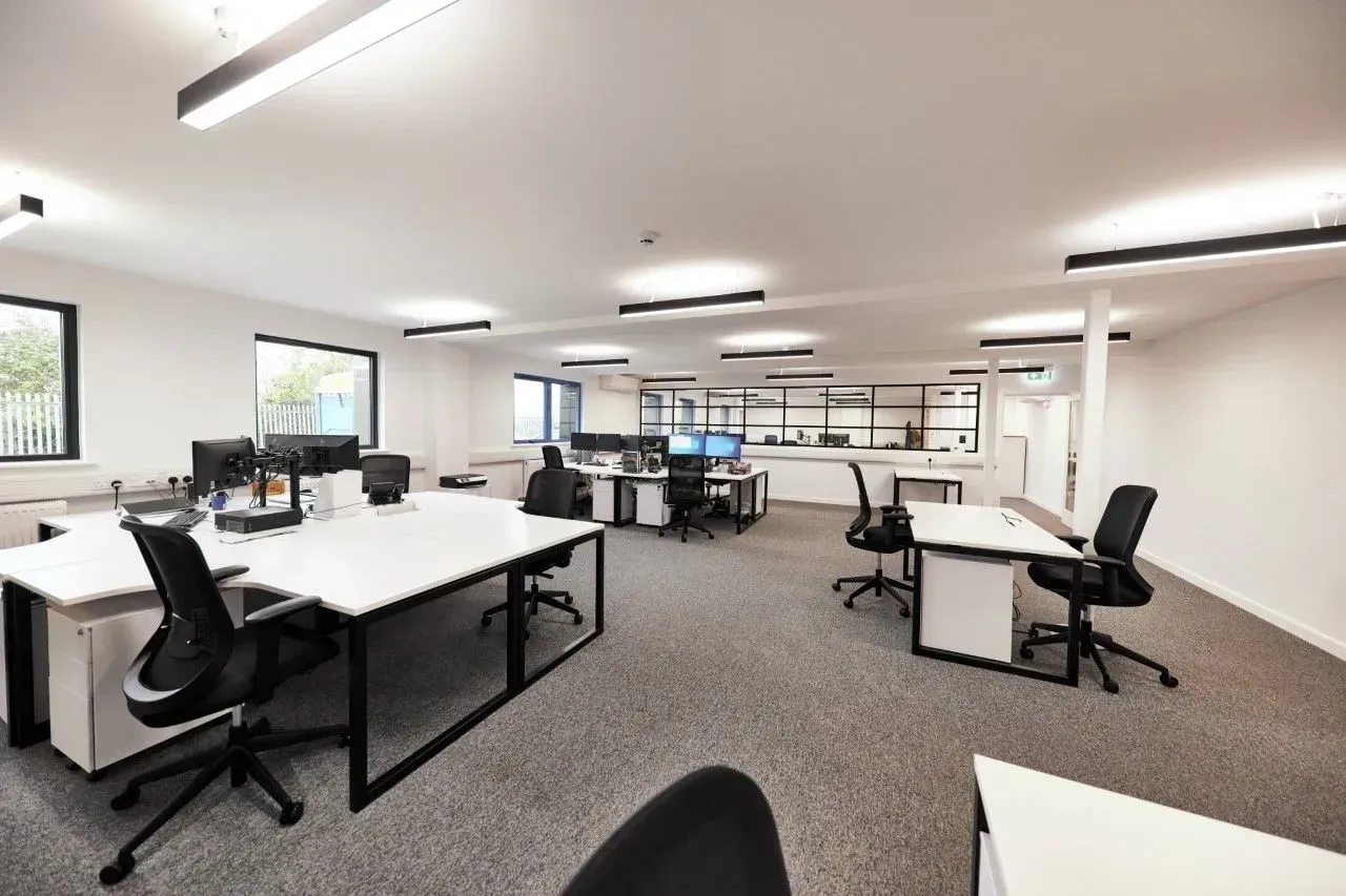 Office with multiple white desks, black chairs, and computers; a modern, well-lit workspace.
