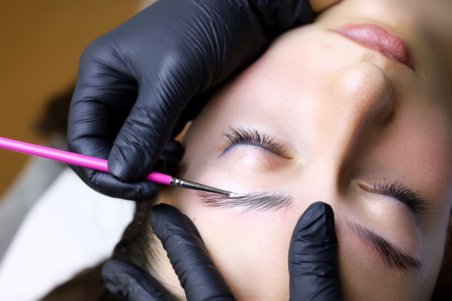 A woman is getting her eyebrows painted by a person wearing black gloves.