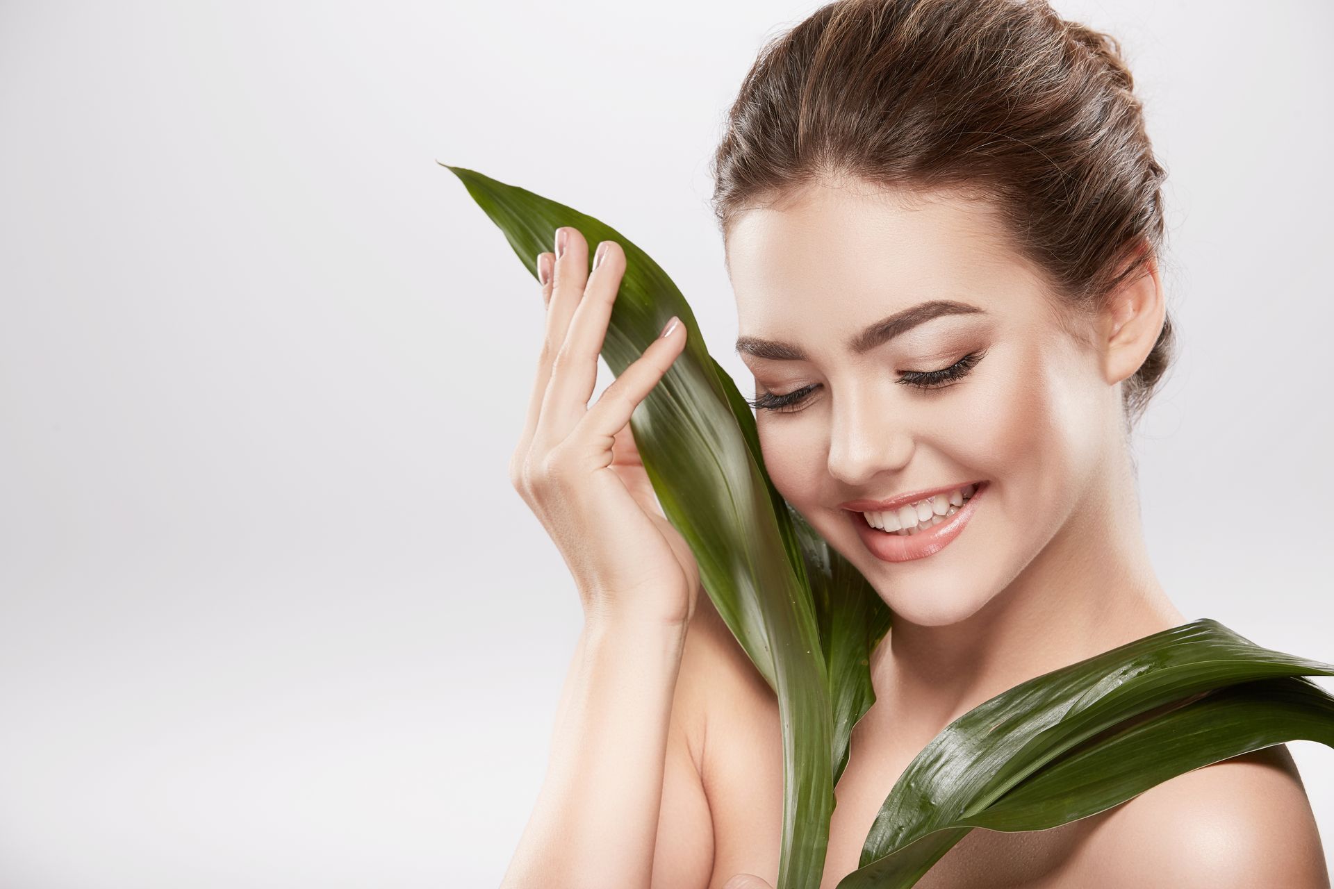 A woman is smiling while holding a green leaf to her face.