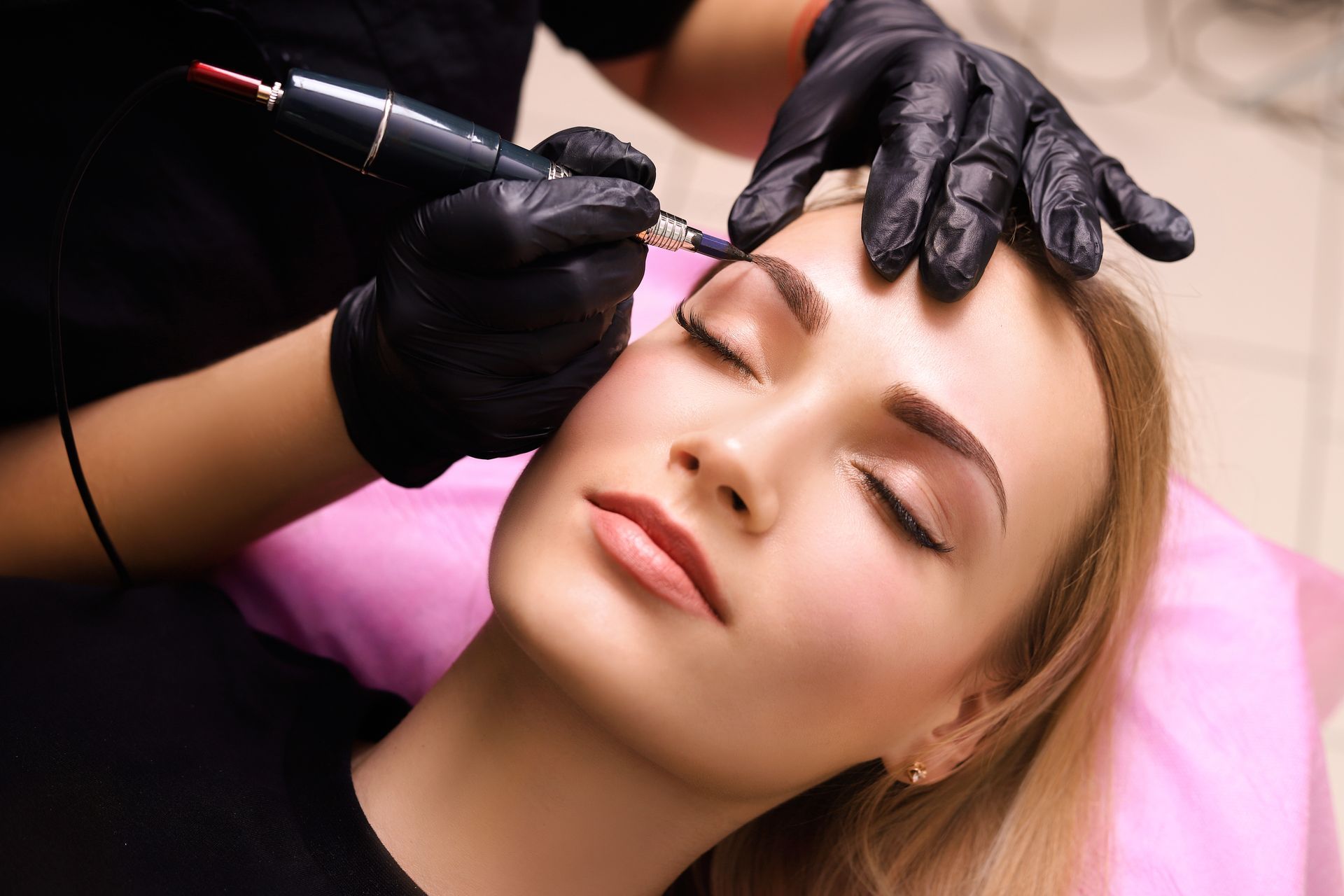A woman is getting a permanent makeup tattoo on her eyebrows.