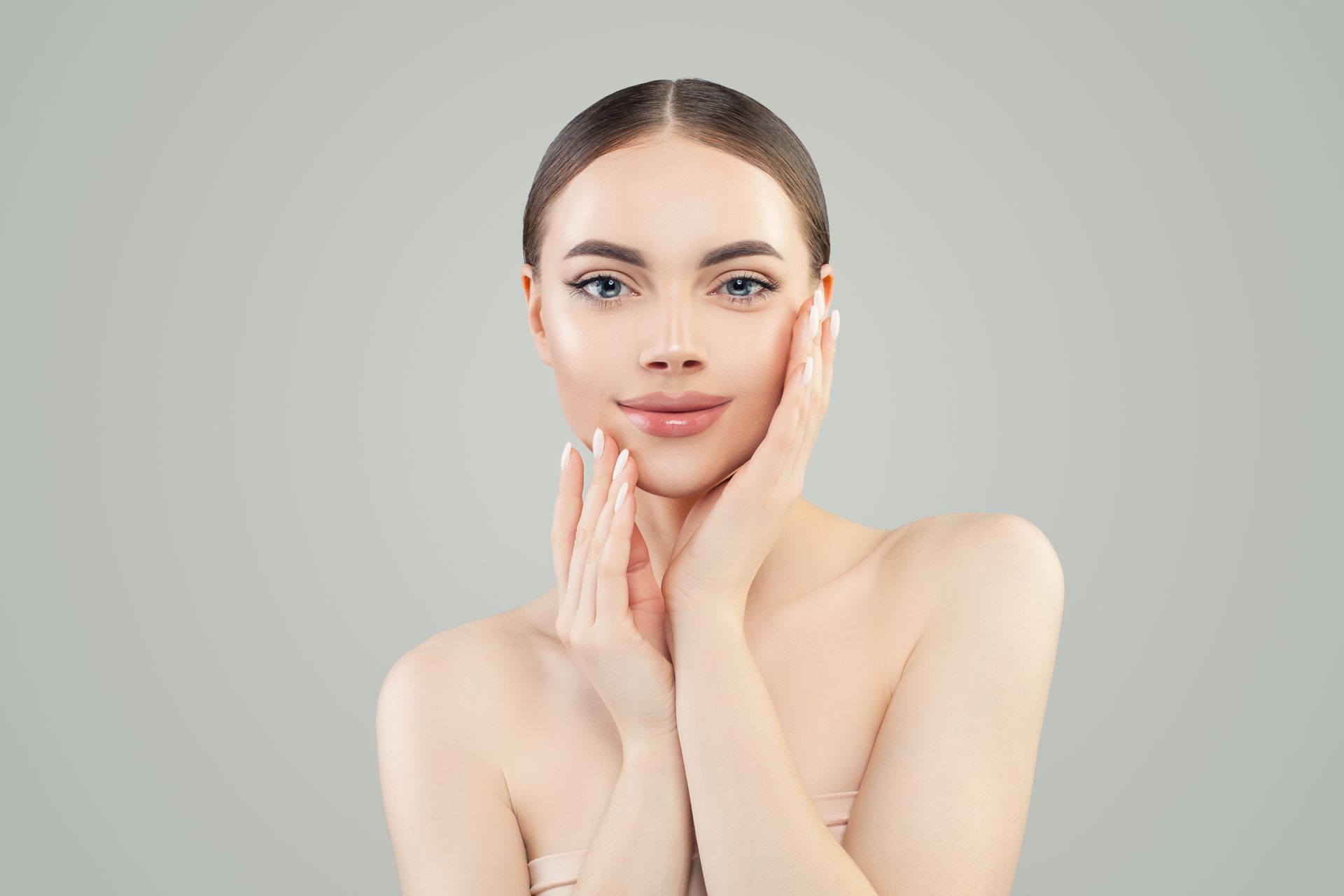 A woman is touching her face with her hands and smiling.
