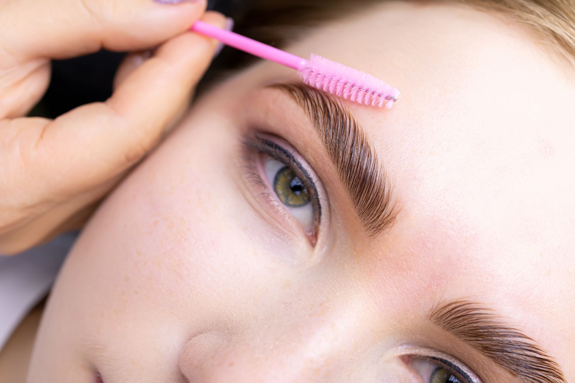 A woman is getting her eyebrows done by a makeup artist.