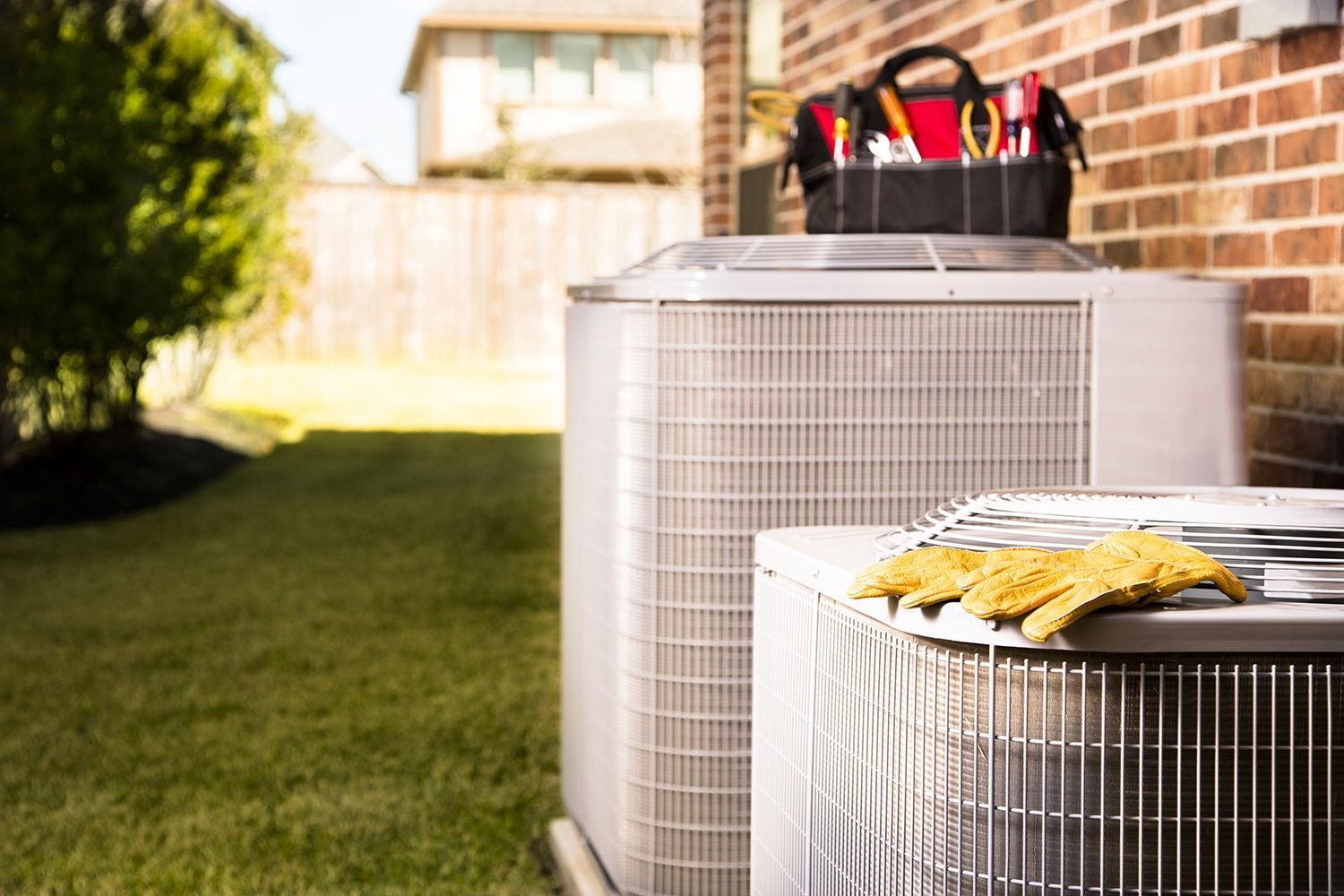 Air conditioning units next to a brick wall with a toolbox, and yard.