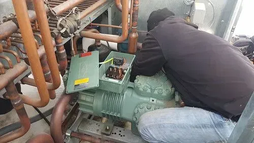 Technician working on green industrial compressor amid copper pipes in a mechanical room
