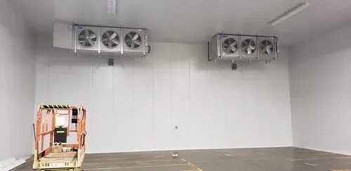 Empty white industrial room with wall-mounted fans and a wooden pallet in the corner