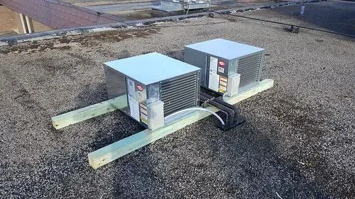 Two silver HVAC units on a gravel rooftop with connected conduits and power cables