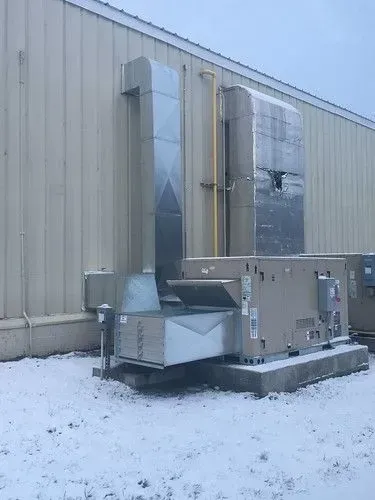 Industrial HVAC equipment beside a beige building on a snowy ground.