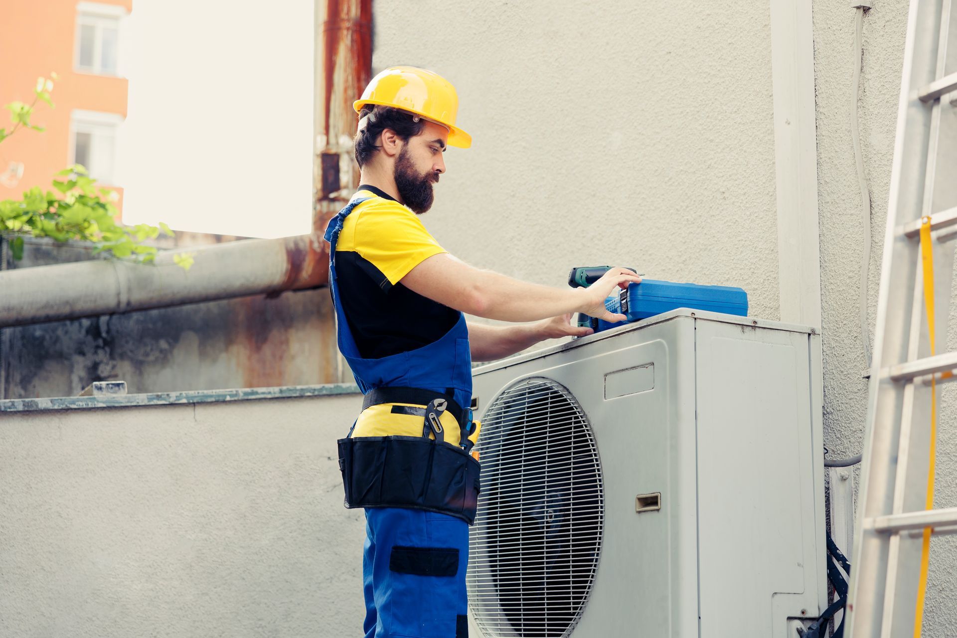 An HVAC technician in a hard hat using a drill to install an outdoor AC condenser unit