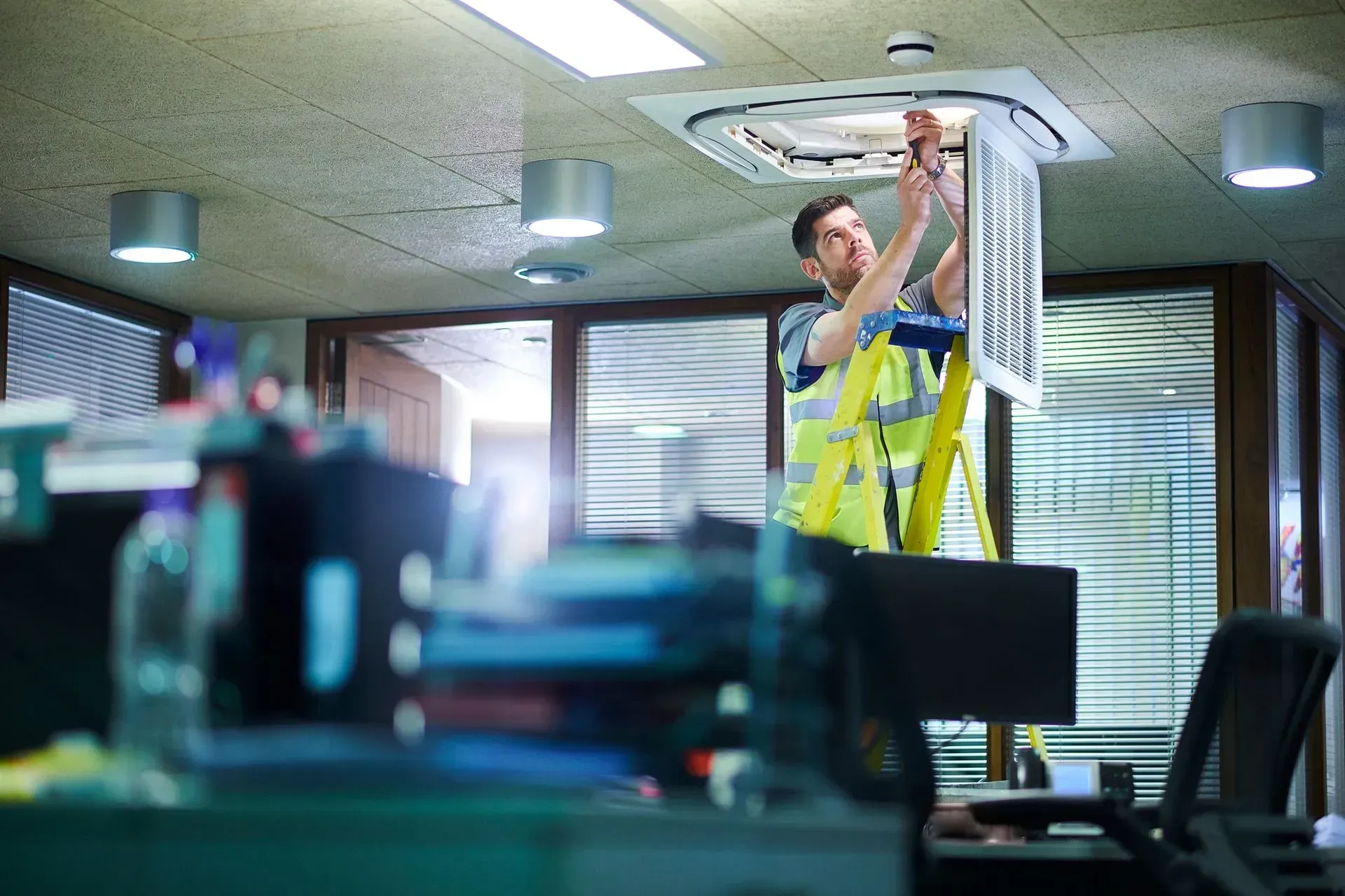 Worker adjusting ceiling light in an office with desks and monitors