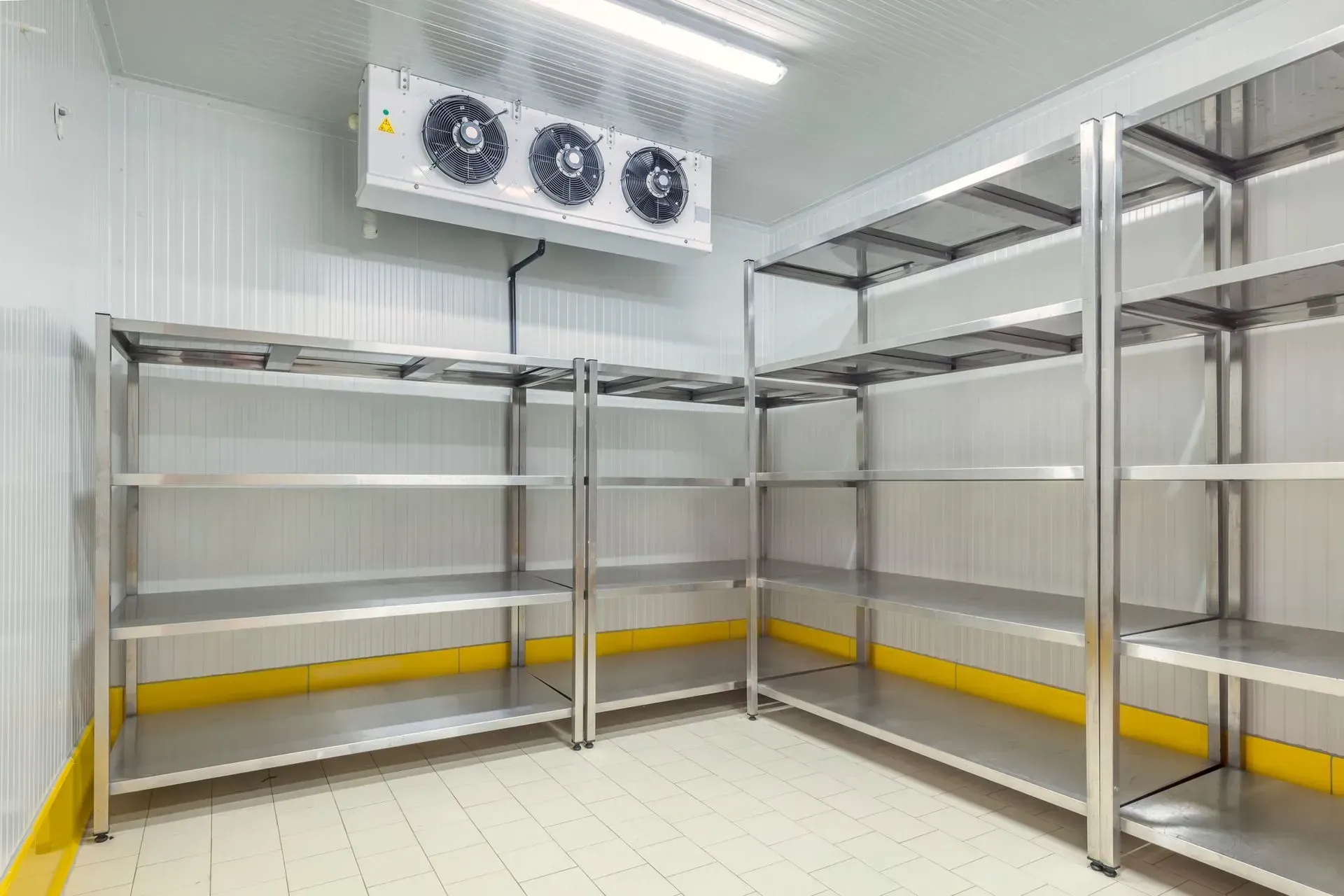Empty industrial cold room with stainless steel racks, white walls, and overhead cooling fans. Empty industrial cold room with stainless steel racks, white walls, and overhead cooling fans.