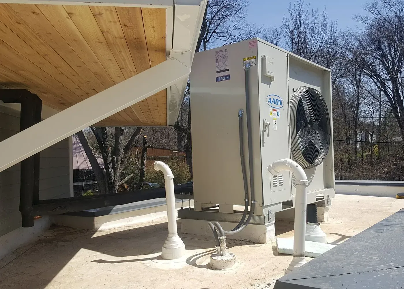 Outdoor HVAC unit beside a building, with pipes and a large fan under a slanted roof. Outdoor HVAC unit beside a building, with pipes and a large fan under a slanted roof.