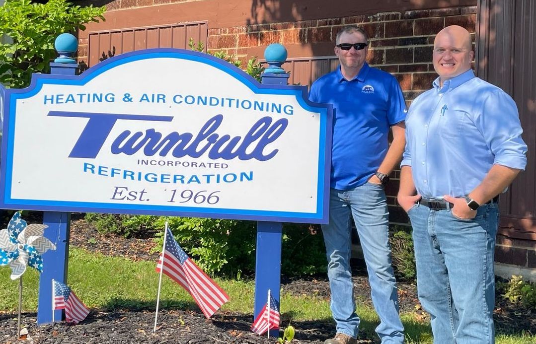 Two men stand by a business sign for Turnbull Heating & Air Conditioning and Refrigeration.