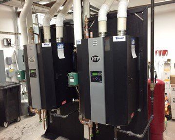 Two black HTP water heaters with white exhaust pipes, copper pipes, and a red expansion tank in a mechanical room.