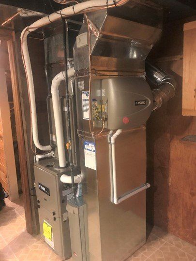 Furnace unit in a basement, with silver metal and white pipes.