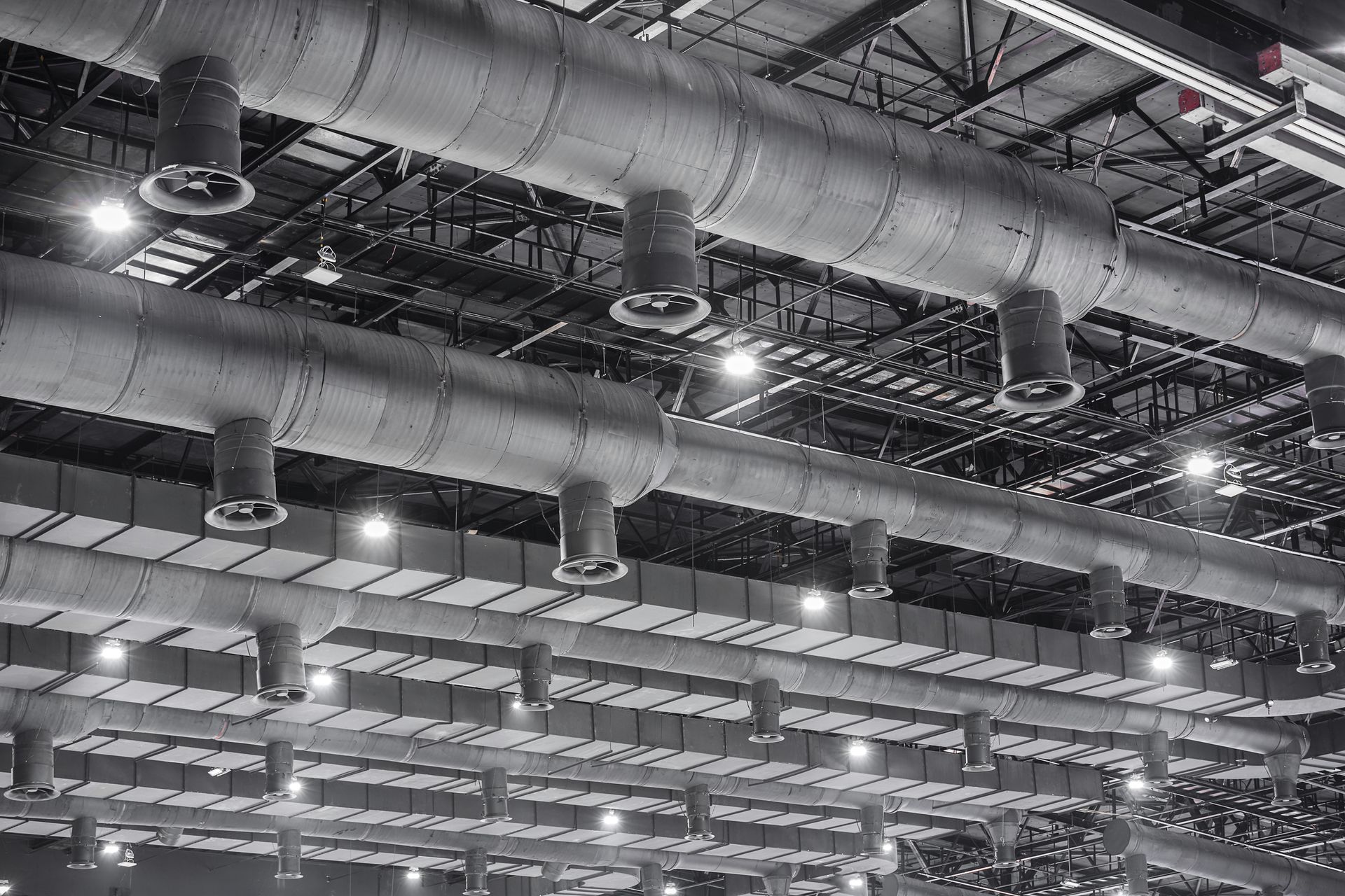 Industrial HVAC ventilation ducts suspended from factory ceiling with exposed steel beams overheads.