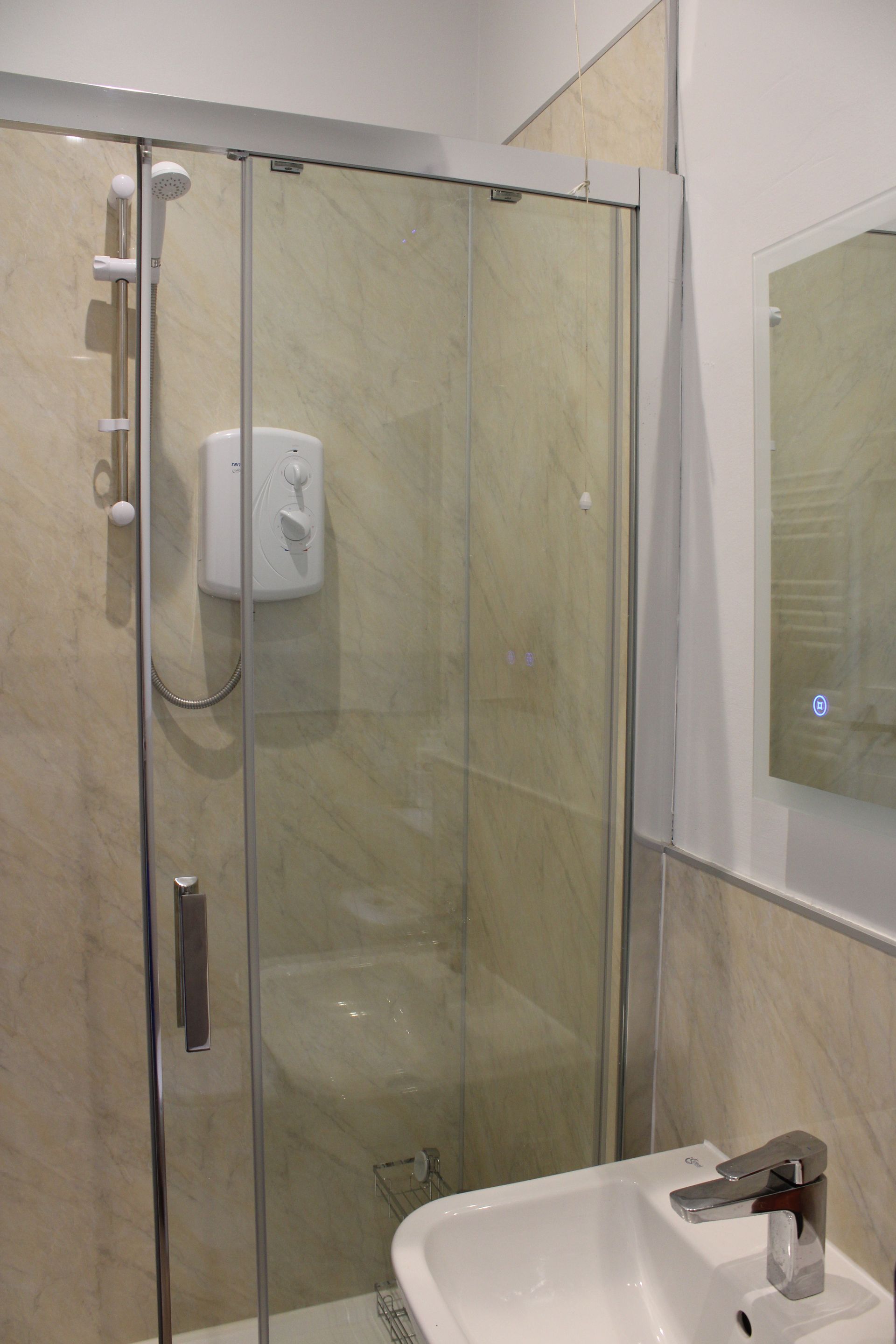 Small bathroom with glass shower stall, wall-mounted dispenser, sink, and mirror.