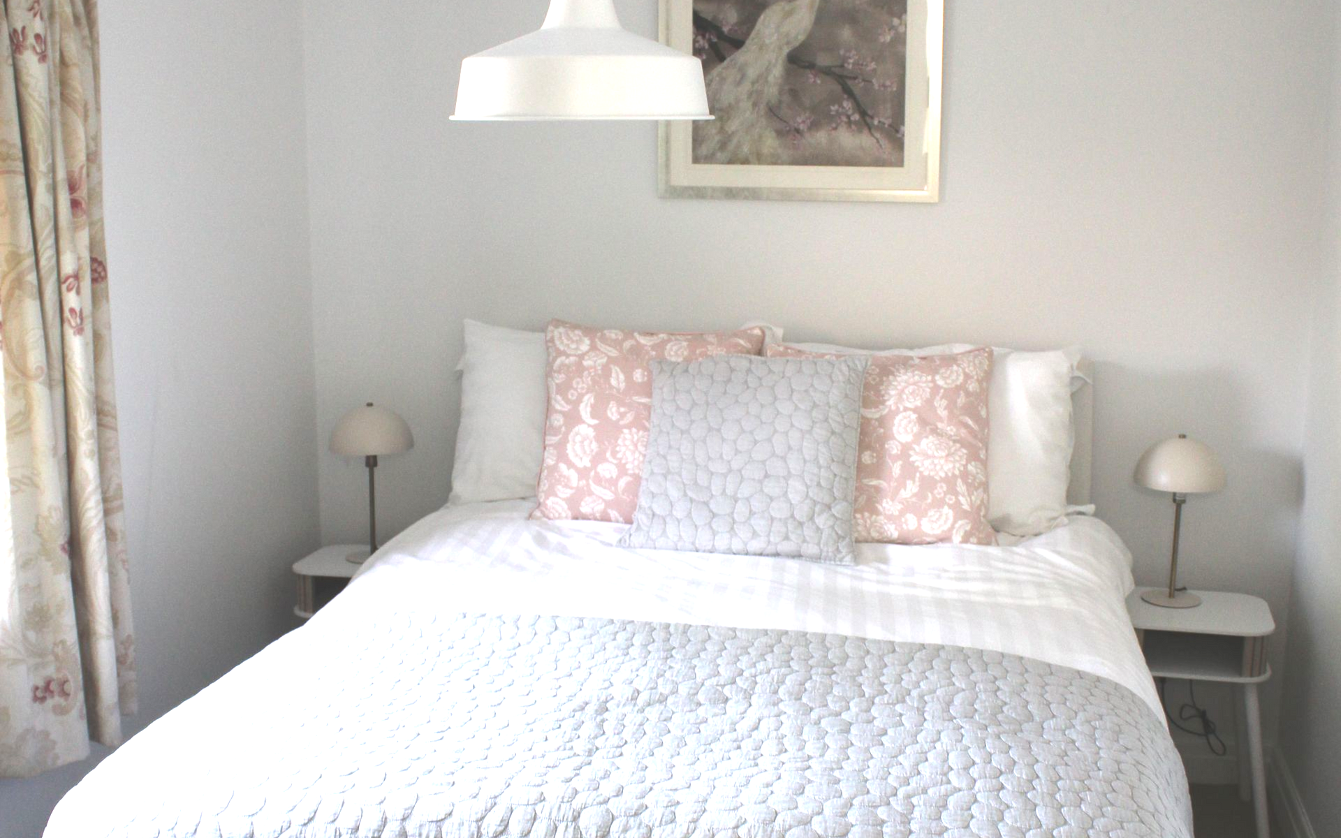Bright bedroom with a white bed, patterned pillows, bedside tables, and a hanging lamp