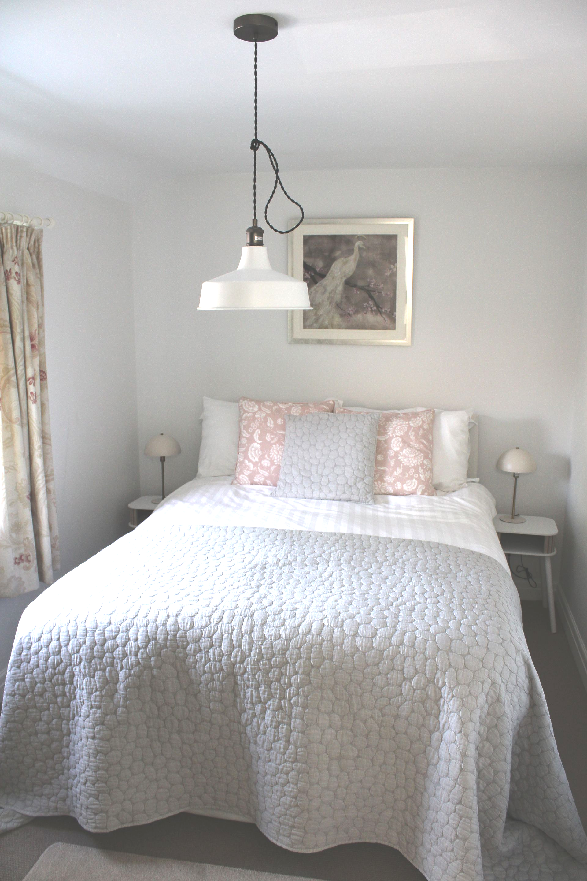 Bright bedroom with a bed, pink pillows, white quilt, hanging lamp, and framed artwork above the headboard