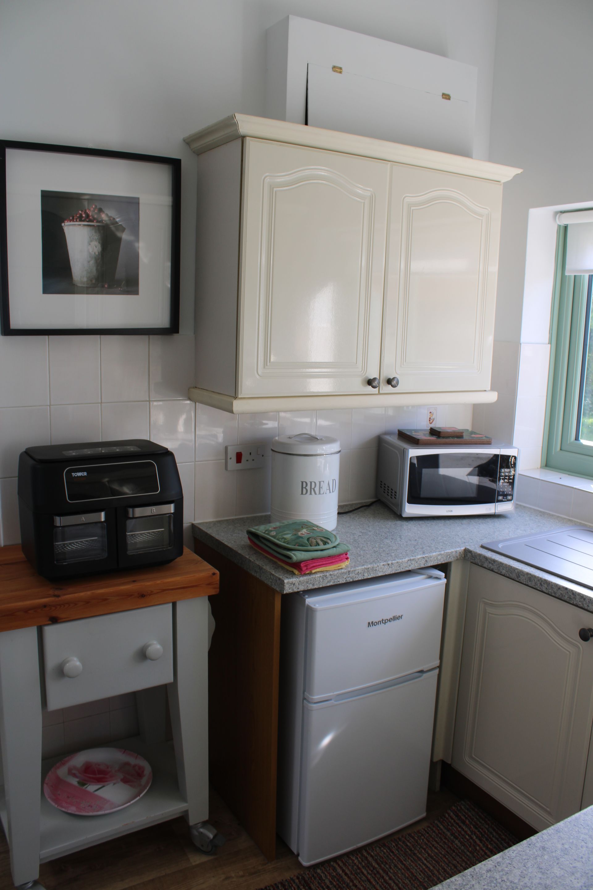 Small kitchen corner with white cabinets, mini fridge, sink, microwave, and countertop appliances.